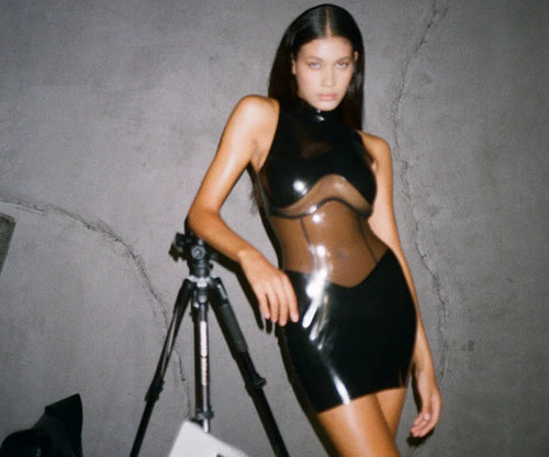 Frau mit einem Latex-Kleid lehnt an Stativ